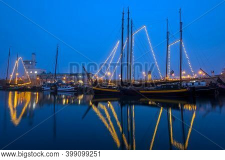 Decorated traditional sailing ships in the harbor from Harlingen in the Netherlands in christmastime at night