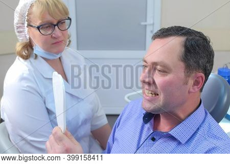 Man Is Looking At Mirror After Cure By Dentist Woman In Dentistry Clinic. Stomatologist Looking At R