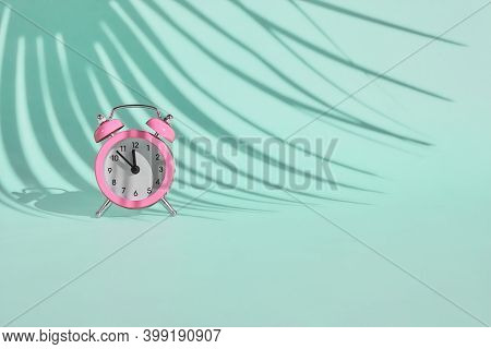 Pink Alarm Clock On Light Blue, Turquoise Pastel Background With A Shadow Of Palm Leaf. Summertime, 