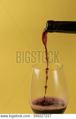Red Wine Is Poured From A Bottle Into A Glass. Yellow Isolated Background.
