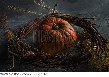 Beautiful Pumpkin Inside A Decorated Wreath Of Twigs And Dry Herbs On A Dark Stone Table