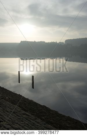 Two Posts Frame The Winters Sun As It Is Reflected In The Calm Water Of A South Yorkshire Reservoir.
