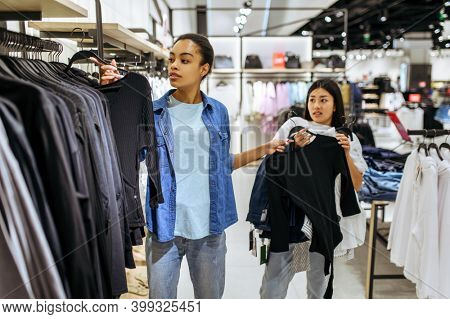 Girls take clothes on hangers in clothing store