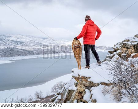 man with classic Huron snowshoes is overlooking a mountain lake in winter scenery - Horsetooth Reservoir in northern Colorado
