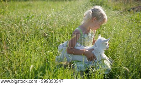 6 Year Old Girl In The Meadow With A Small White Goat.