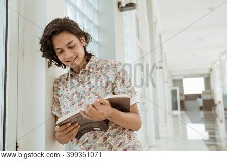 Portrait Of Happy Male Student Reading Holding Book