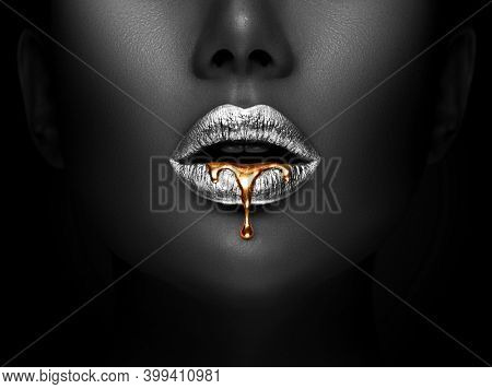 Golden lipstick closeup. Liquid metal dripping from silver lips. Beautiful makeup. Sexy lips, bright liquid paint on beauty African American model girl's mouth, close-up. Lipstick.