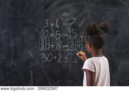 Beautiful Mixed Race Schoolgirl Standing In Front Of A Chalkboard, Solving Math Equations, Practisin