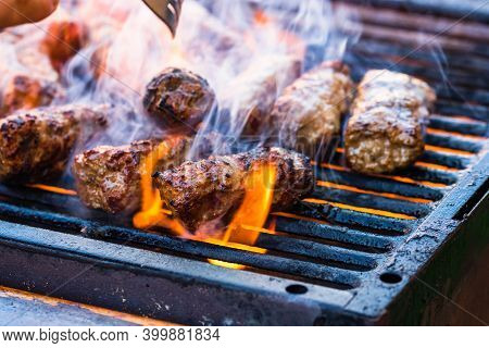 Preparing Meat Rolls Called Mici Or Mititei On Barbecue. Close Up Of Grill With Burning Fire With Fl