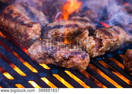 Preparing Meat Rolls Called Mici Or Mititei On Barbecue. Close Up Of Grill With Burning Fire With Fl
