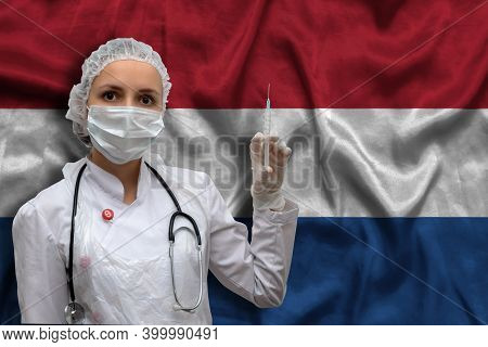 Young Woman Doctor In Medical Uniform On The Background Of The National Flag Of Netherlands Is Holdi