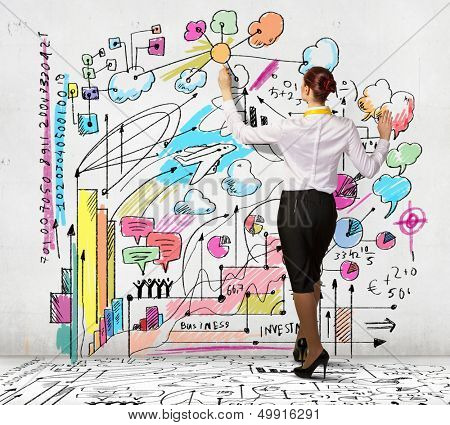 Businesswoman standing with back drawing business ideas on wall
