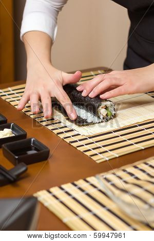 Woman hand moistening with water a sushi roll edge