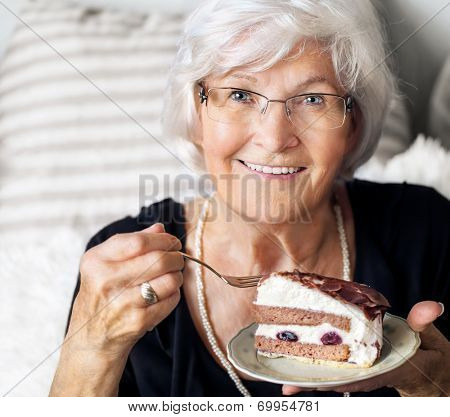 Senior lady looking happy at camera, she likes to eat a piece of cream cake 