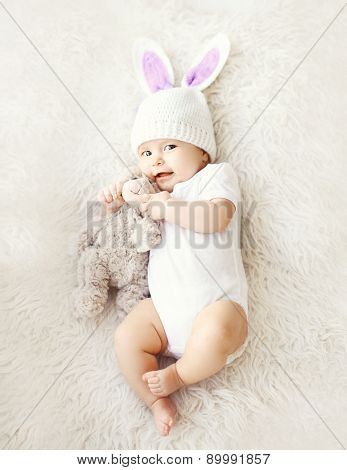 Soft Photo Of Sweet Cute Baby In Knitted Hat With A Rabbit Ears And Teddy Bear Lying On The Bed, Top