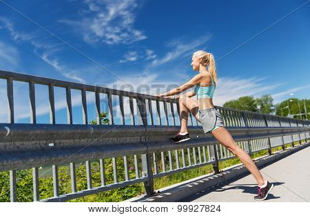 fitness, sport, exercising and healthy lifestyle concept - smiling woman stretching leg outdoors