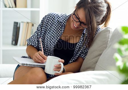Beautiful young woman writting on the notebook while drinking coffee.