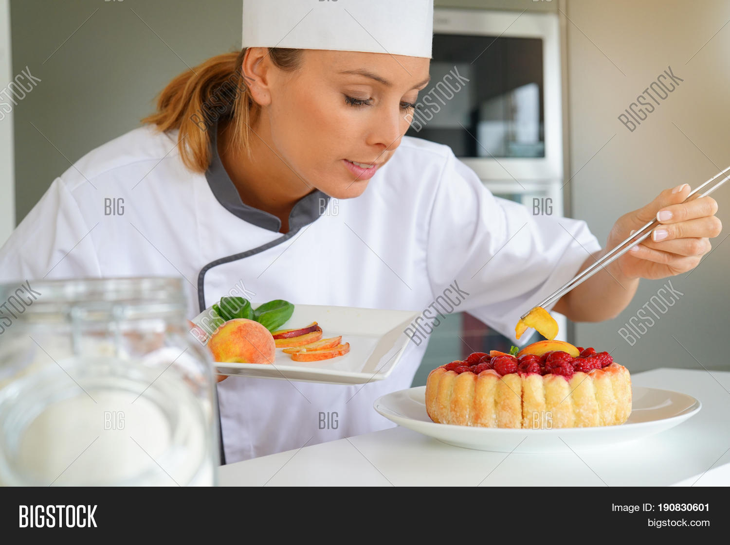 pastry chef in professional kitchen decorating raspberry cake