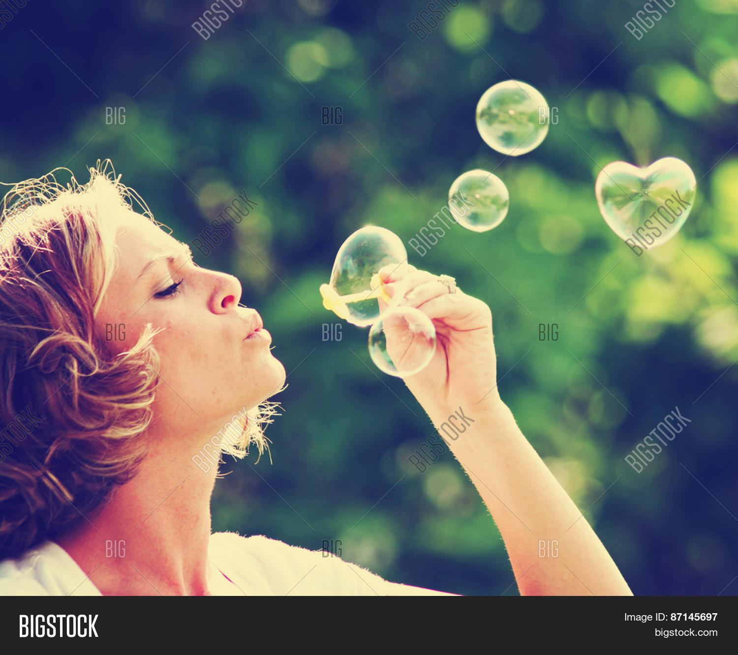 a beautiful woman blowing bubbles (one in the shape of a heart)