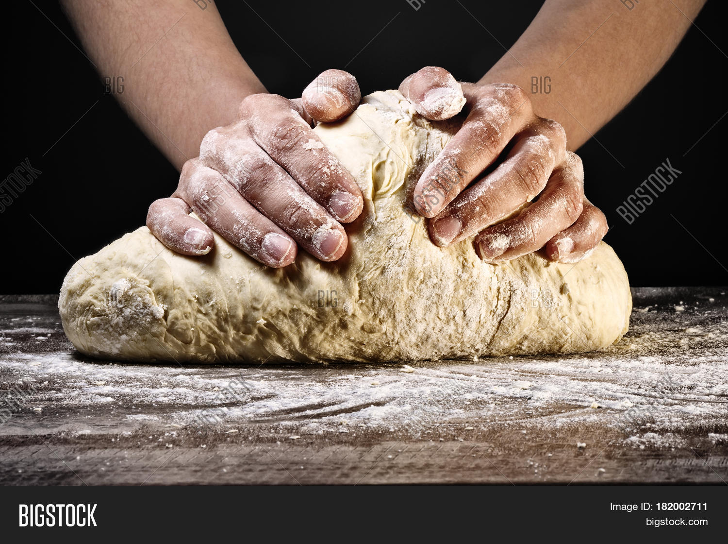 womans hands kneading the dough on dark background.