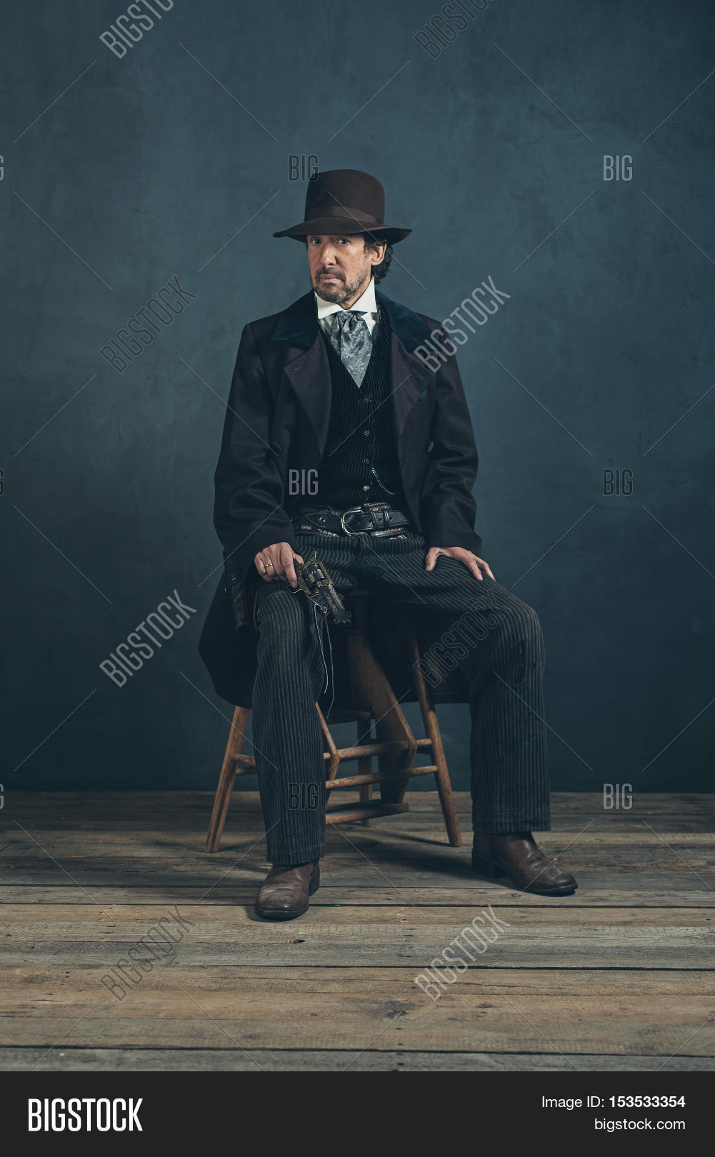 vintage 1900 western mature man with revolver sitting on wooden