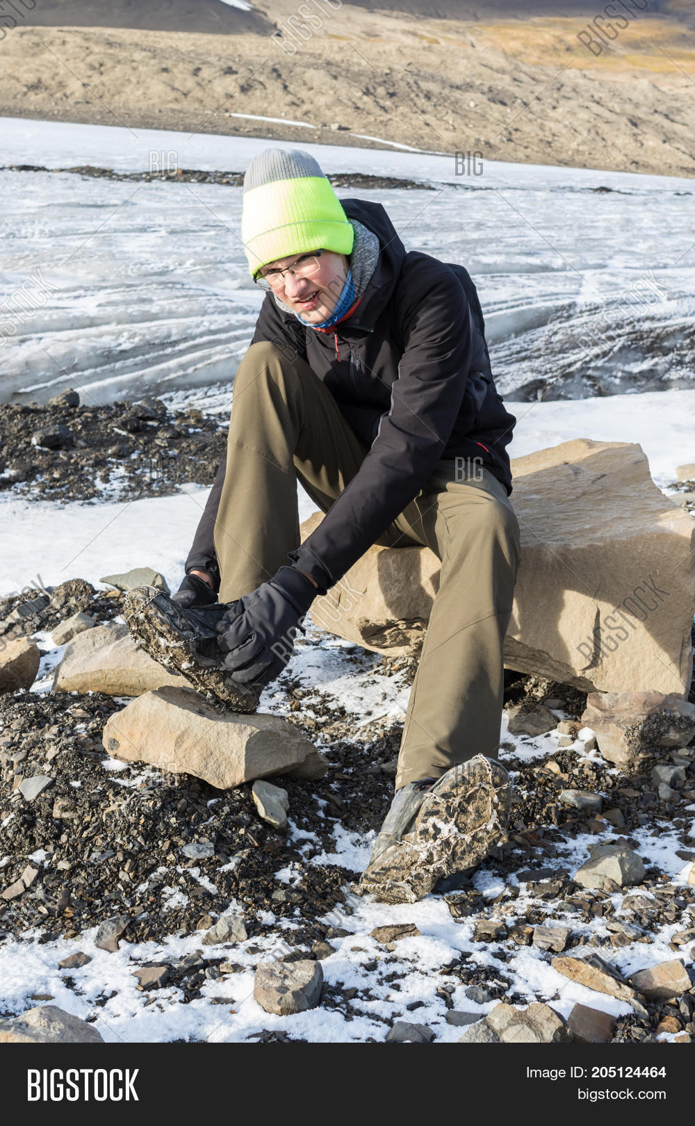 teenager attaching ice spikes to his shoes to walk on glacier.