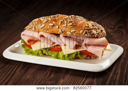 ham sandwich with lettuce, cheese, tomato on plate on wooden