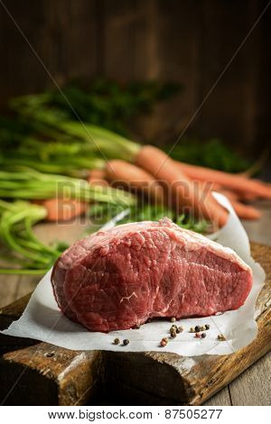joint of raw topside beef with carrots in the background