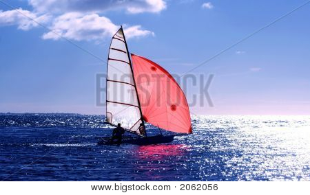 Red Sail, dinghy sailing into the sun on a blue sea : Bigstock