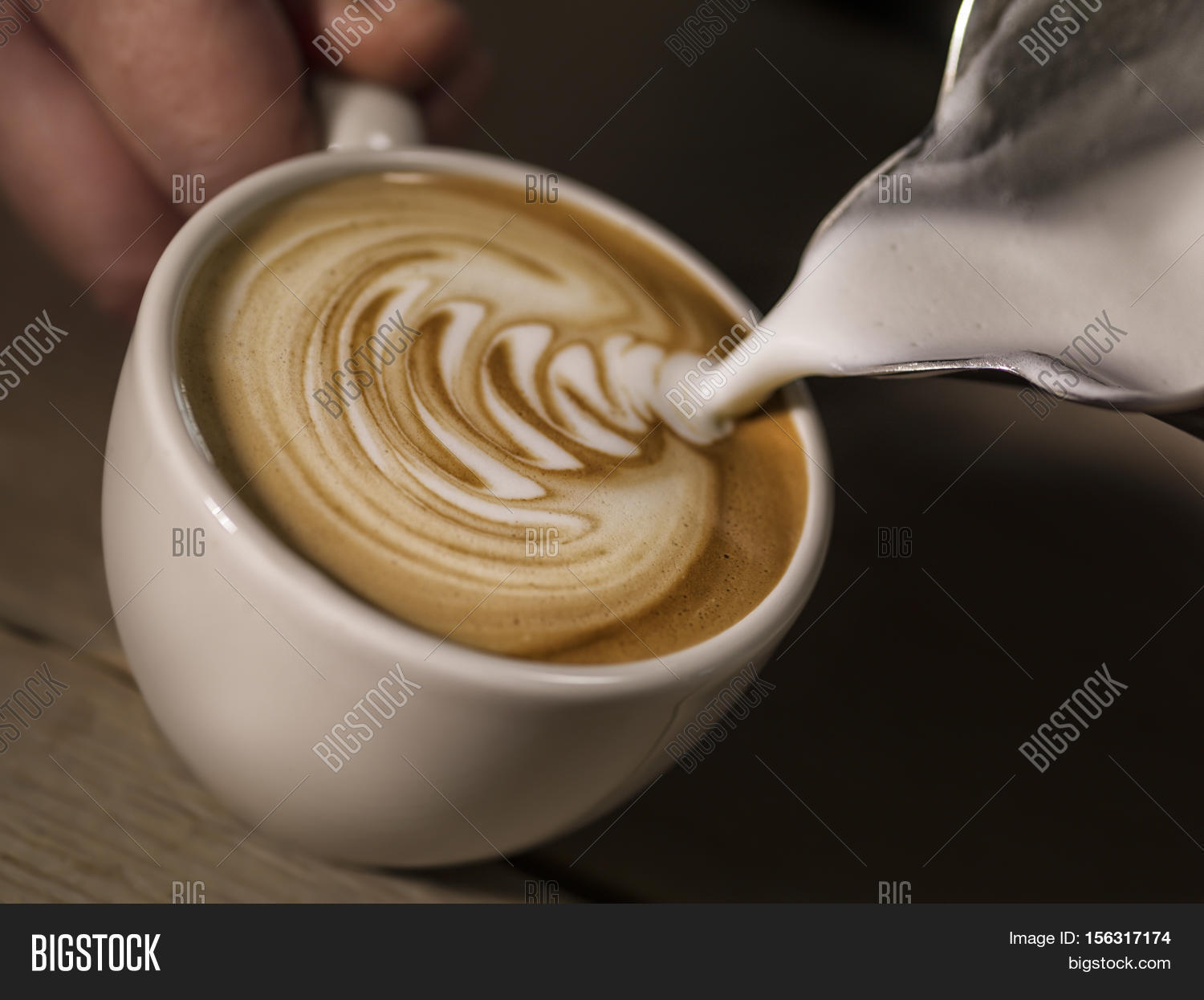 hand of barista making latte or cappuccino coffee pouring milk