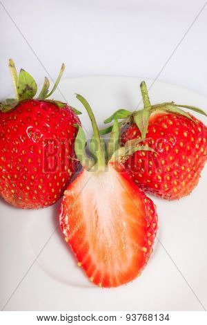 half of ripe and juicy strawberries on a plate with two whole