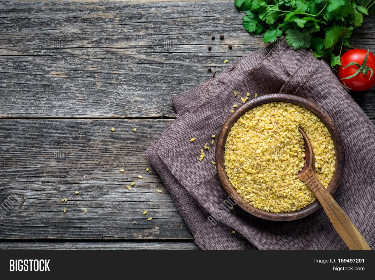 bulgur (dry wheat grains) in wooden bowl, fresh parsley, tomato