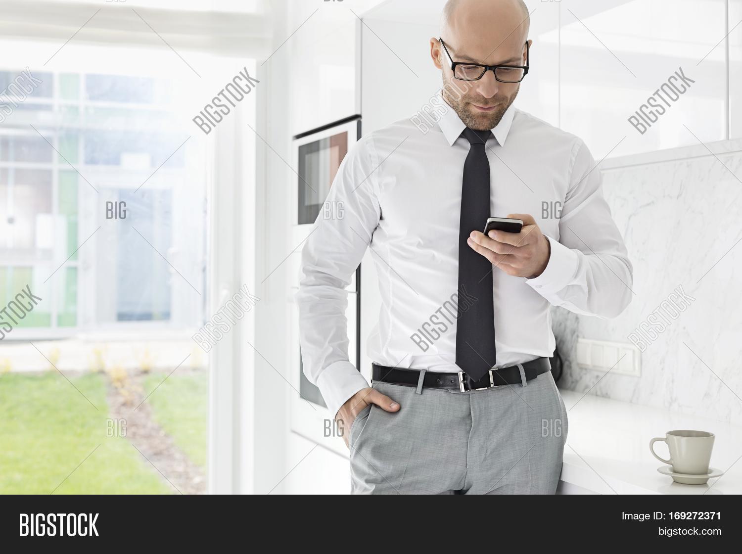 mid adult businessman text messaging through smart phone at home