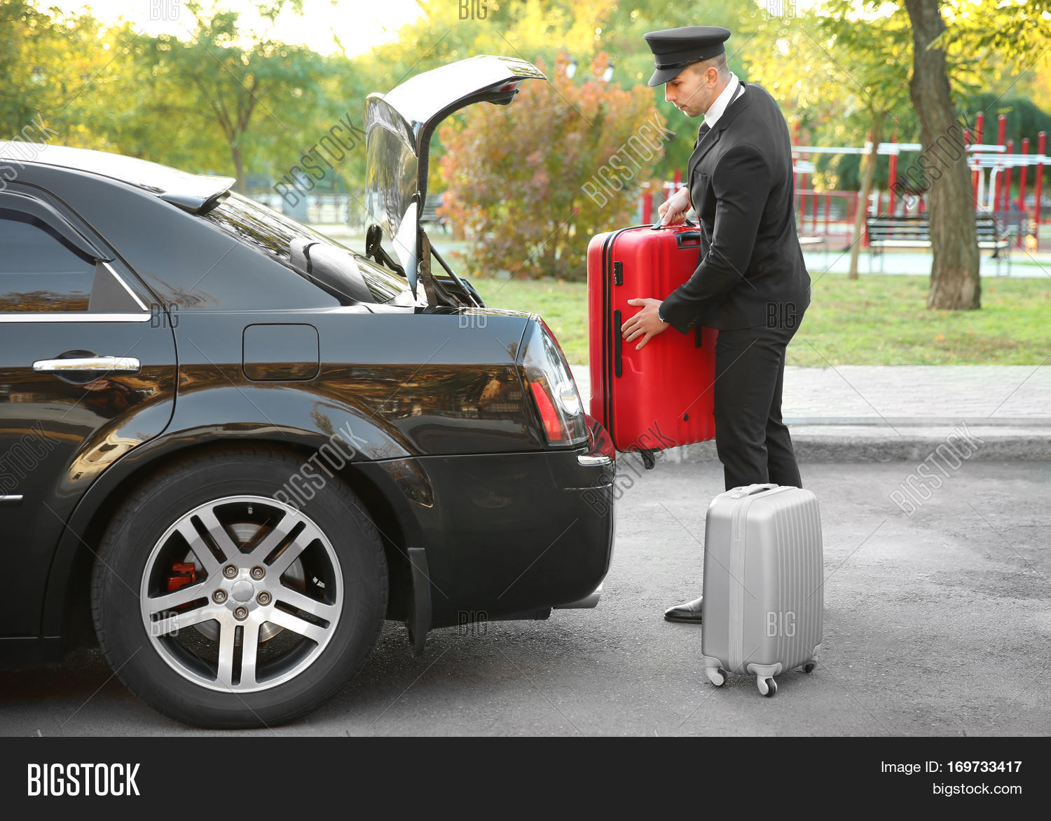 chauffeur putting suitcase in car trunk